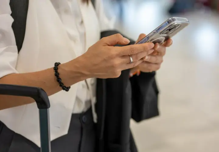 Kobieta z telefonem w dłoni, obok walizki. Sprawdza informacje o wyłączeniu 3G Plus, przygotowując się do podróży.