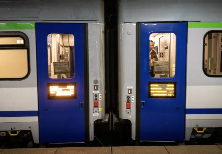 Dwa wagony kolejowe z niebieskimi drzwiami i oknami. Widać numery wagonów 16 i 15. Różne rodzaje wagonów czekają na pasażerów.