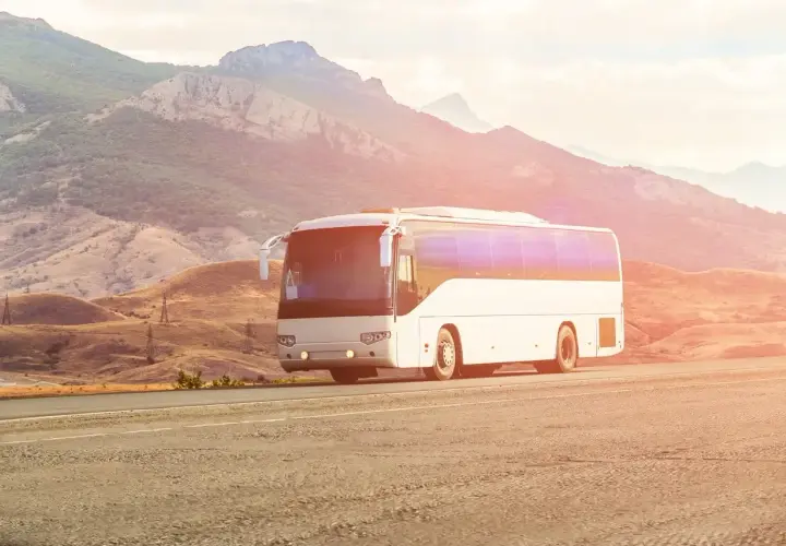Biały autokar jedzie drogą w malowniczym, górzystym krajobrazie. Kierowca autobusu wiezie pasażerów w podróż.