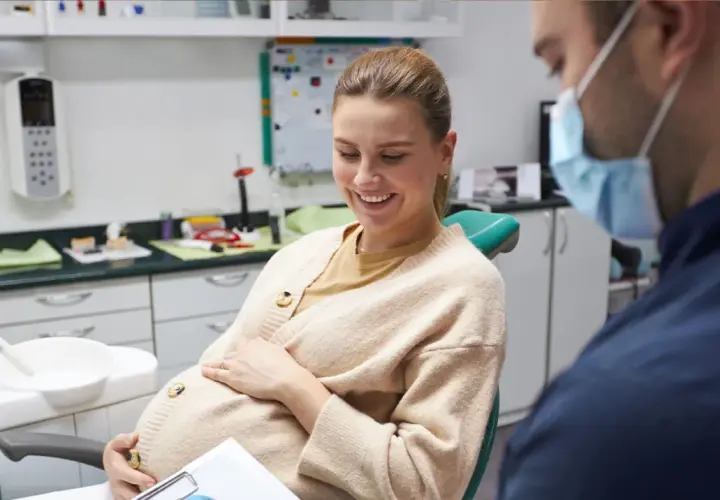 Donna incinta sorride dal dentista, preoccupata per la carie in gravidanza.