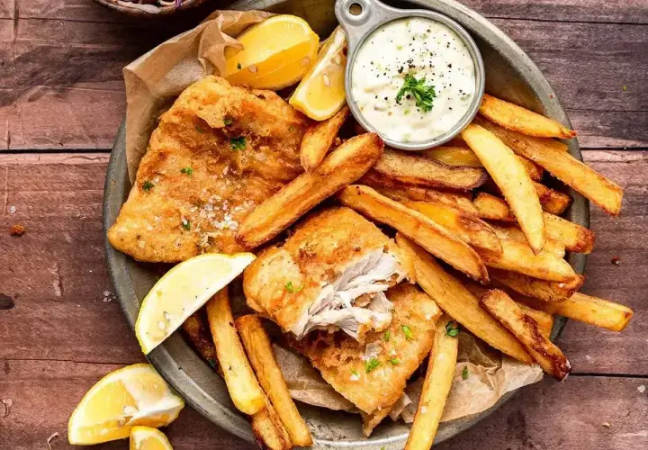 Chrupiące **fish and chips** z cytryną i sosem tatarskim na drewnianym stole. Idealna przekąska!