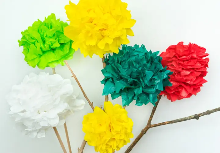 Bunte Seidenblumen basteln: Fünf Papierblumen in Rot, Grün, Gelb und Weiß auf Holzästen vor weißem Hintergrund.