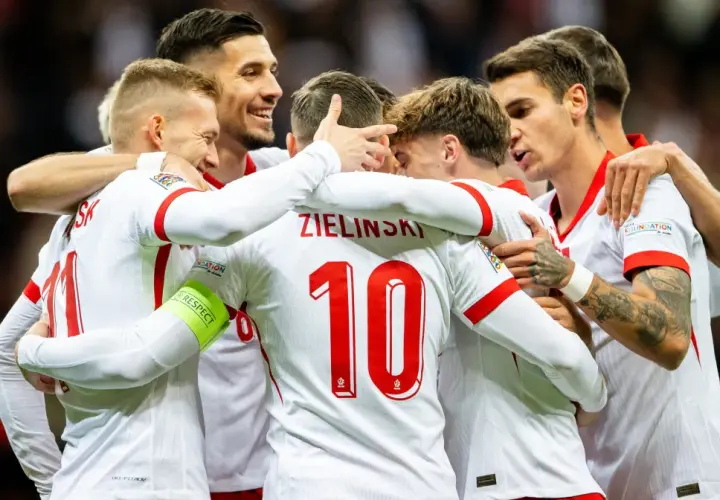 Piłkarze reprezentacji Polski w białych strojach świętują razem, przytulając się.