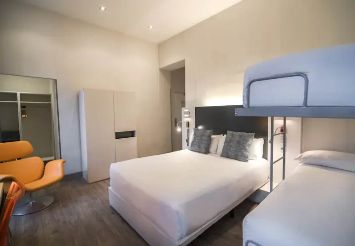 Habitación familiar en Petit Palace Canalejas Sevilla con cama doble, litera y sillón naranja.