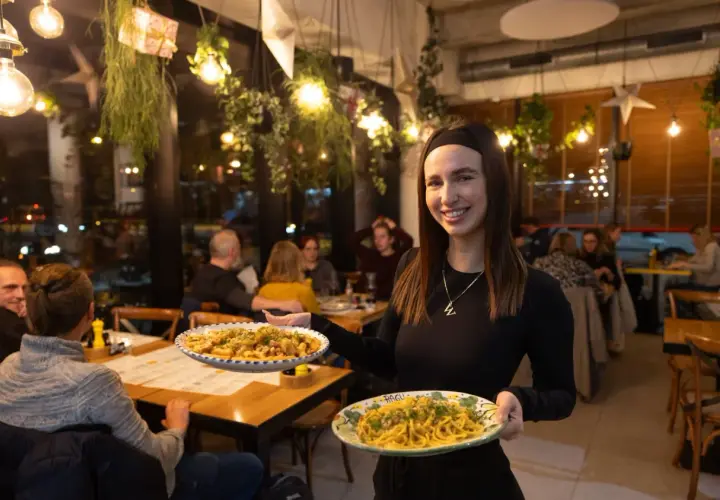 Uśmiechnięta kelnerka serwuje pyszne dania w najlepszej włoskiej restauracji we Wrocławiu. Aromatyczne makarony kuszą z talerzy.