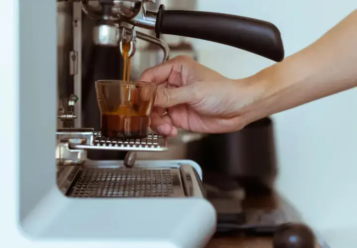 Eine Hand hält ein Glas, während frisch gebrühter Espresso manuell zubereitet wird.