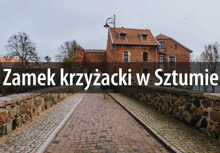 Kamienny most prowadzi do ceglanego zamku krzyżackiego w Sztumie. W oddali widać drzewa i pochmurne niebo.