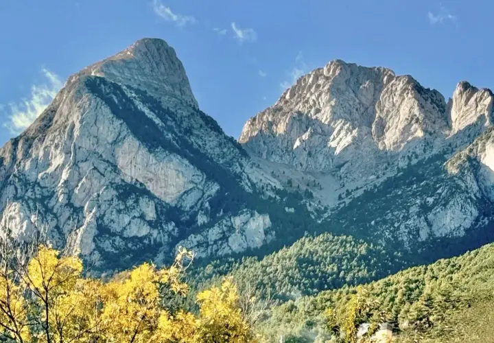 Majestuosas montañas de el Pedraforca bajo un cielo azul. El sol ilumina las cumbres rocosas y los bosques verdes.