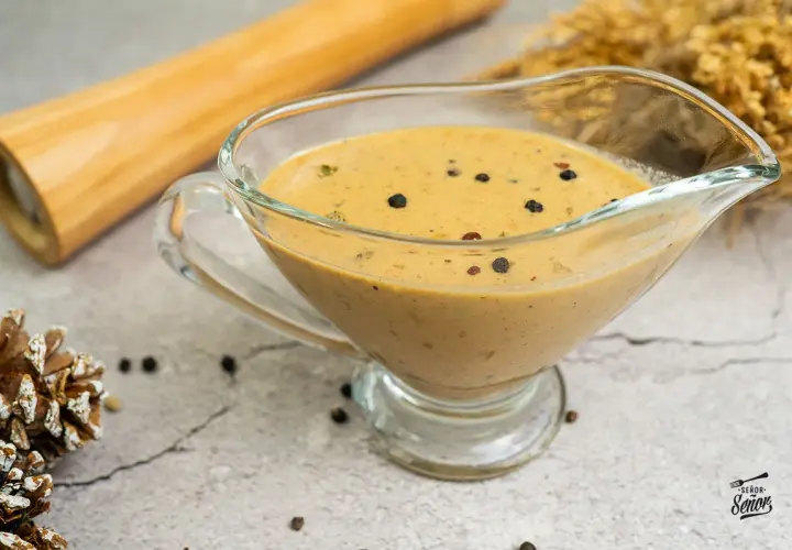 Salsa a la pimienta cremosa en una salsera de cristal, con granos de pimienta negra esparcidos.