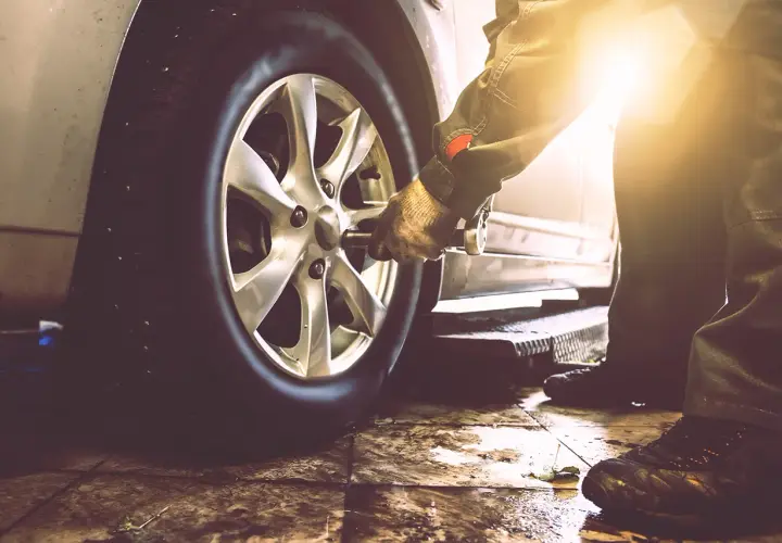 Mechanik w rękawicy używa klucza do odkręcenia koła samochodu. Pokazane jest, jak odkrecic kolo.