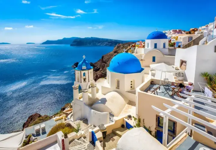 Błękitne kopuły kościołów na Santorini nad lazurowym morzem. Takie morze jest w Grecji, idealne na wakacje.