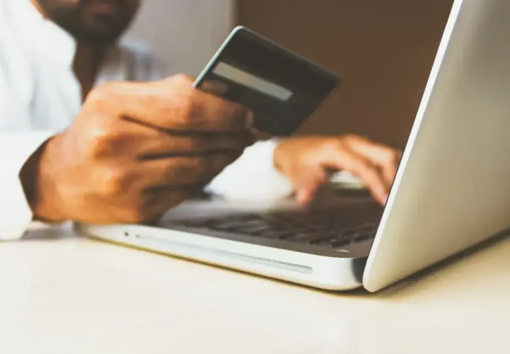 Mężczyzna z kartą kredytową w dłoni wpisuje dane na laptopie, realizując swój hedonizm w zakupach online.