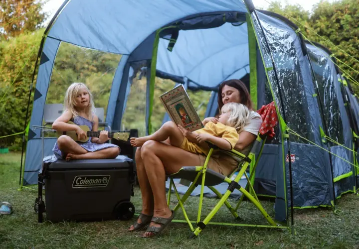 Mama czyta dzieciom w namiocie w Polsce. Jedno dziecko gra na ukulele, drugie słucha bajki. Idealne miejsce, gdzie pod namiot z dziećmi w Polsce.