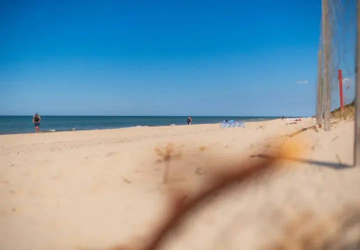Słoneczna plaża w Niechorzu, idealne miejsce na relaks. W oddali widać ludzi spacerujących brzegiem morza.