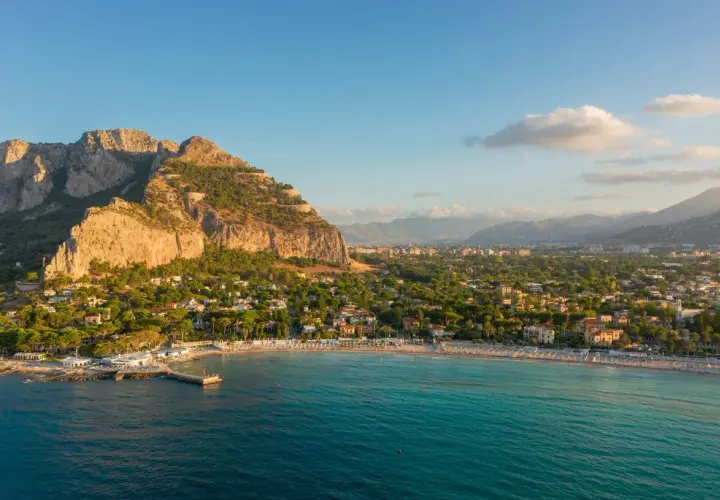 Vista aerea del mare di Palermo con la costa, la spiaggia affollata e le montagne sullo sfondo.
