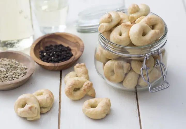 Taralli que es: crujientes bocaditos horneados, algunos en un frasco, con granos de pimienta y hinojo cerca.