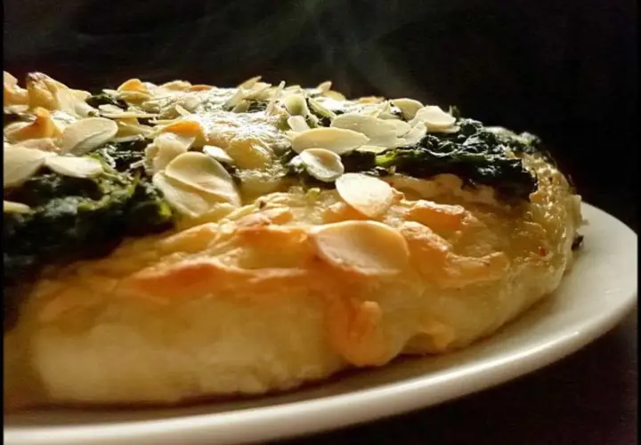 Eine köstliche Spinat Pizza mit knusprigem Teig und gerösteten Mandelblättchen. Dampf steigt auf und verspricht ein warmes, herzhaftes Gericht.