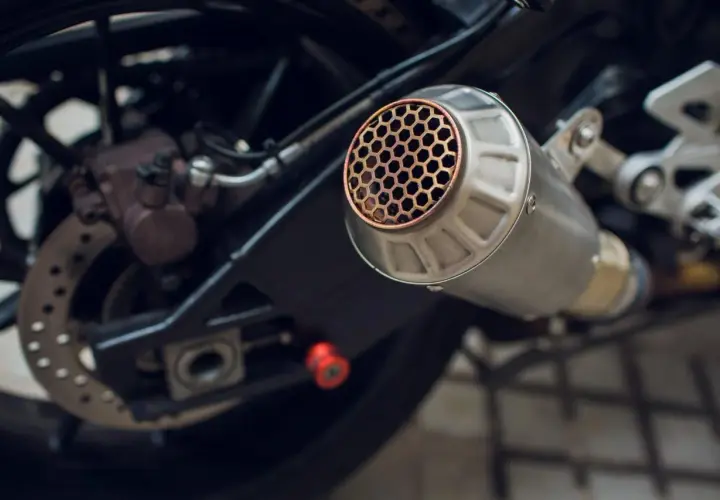Scarico moto con griglia a nido d'ape, un **db killer fai da te** per un suono più discreto. Si intravede la ruota posteriore e il freno.