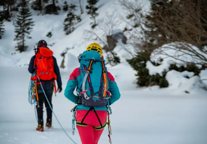 Dwóch alpinistów w zimowych strojach, z plecakami i sprzętem, przemierza ośnieżony teren. To inspiracja, co zabrać w góry zimą.