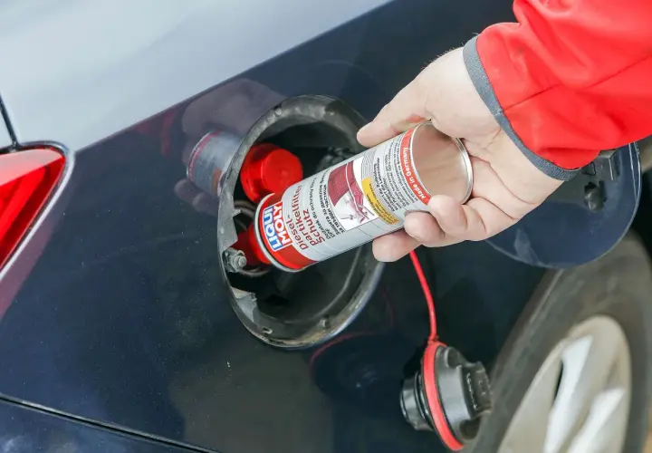 Ręka wlewa dodatek do diesla DPF do baku samochodu. Preparat chroni filtr cząstek stałych.