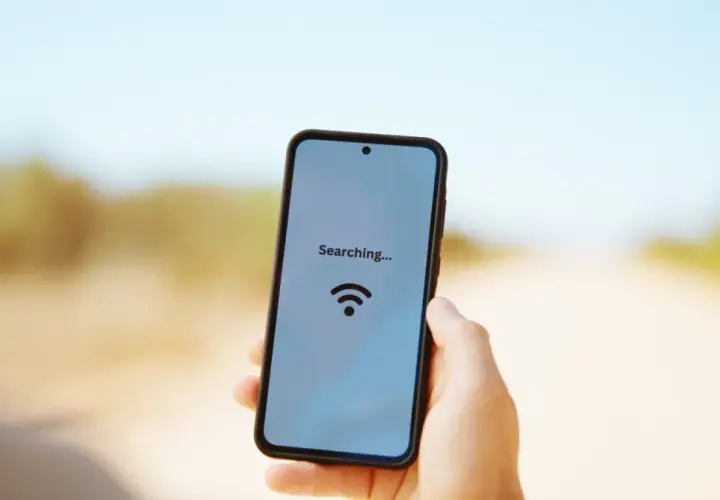 Dłoń trzyma smartfon z napisem "Searching..." i ikoną Wi-Fi na tle drogi.