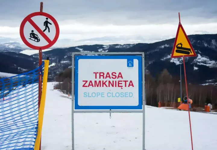 Na stoku narciarskim widoczne są wskaźniki kolejowe: zakaz saneczkarstwa, tablica "Trasa zamknięta" oraz znak ostrzegawczy z ratrakiem.