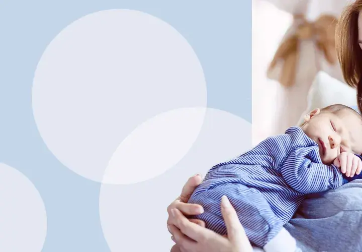 Uśmiechnięta mama tuli śpiącego noworodka w pasiastym pajacyku. Idealny strój na pierwsze wyjście ze szpitala.