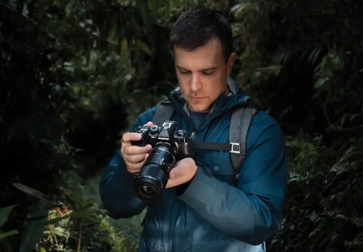 Mężczyzna w lesie trzyma aparat OM-1 Olympus, przygotowując się do makrofotografii sprzętu.