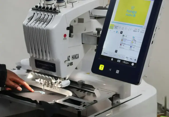 Une machine à broder professionnelle, type impression DTG, crée un logo sur un tissu. L'écran tactile affiche les détails du projet.