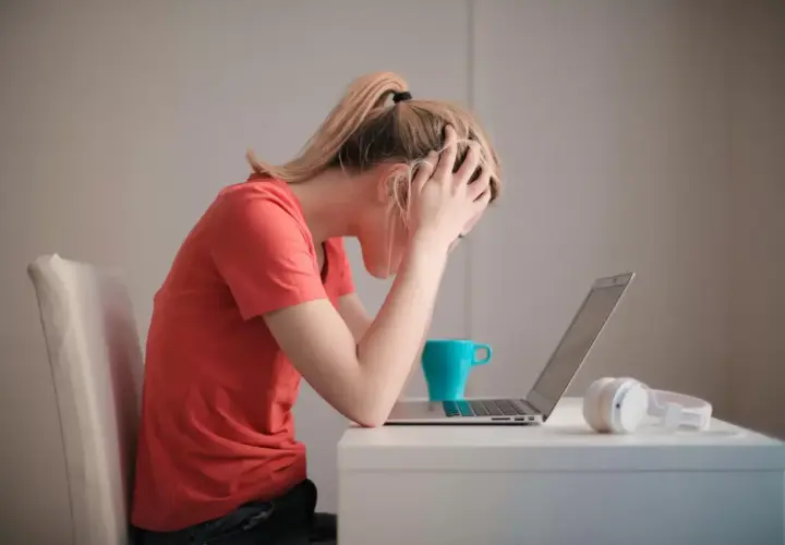 Donna con le mani tra i capelli, frustrata davanti al laptop. La cistite è rabbia repressa, un peso che schiaccia.