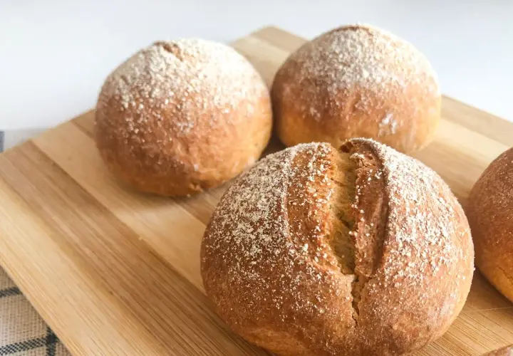 Pane dorato e fragrante, appena sfornato nella friggitrice ad aria, cosparso di farina su un tagliere di legno.
