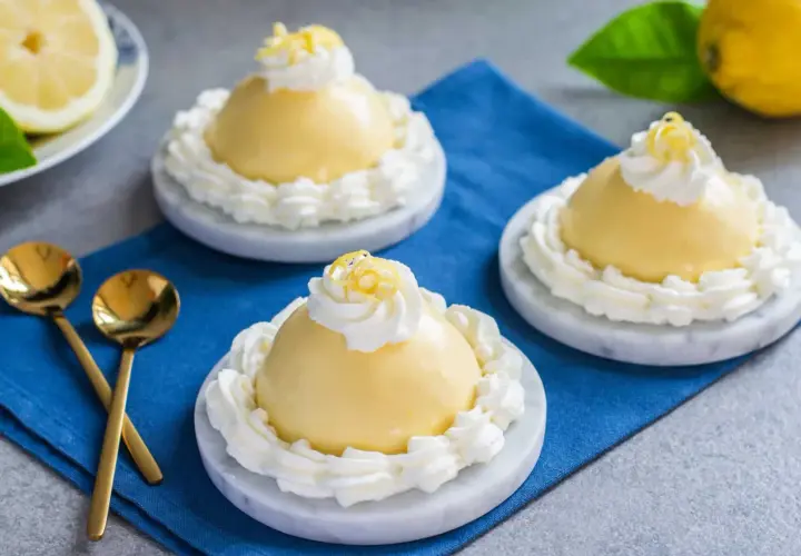 Tre deliziose delizie al limone, guarnite con panna montata e scorza di limone, su piattini di marmo.
