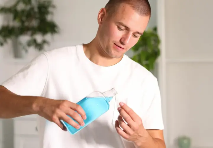 Uomo versa collutorio blu in un misurino. Curasept a cosa serve? Per un alito fresco e una bocca sana.