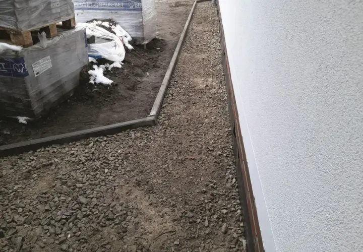 Niedokończony podjazd do domu, z paletami kostki brukowej i żwirem.