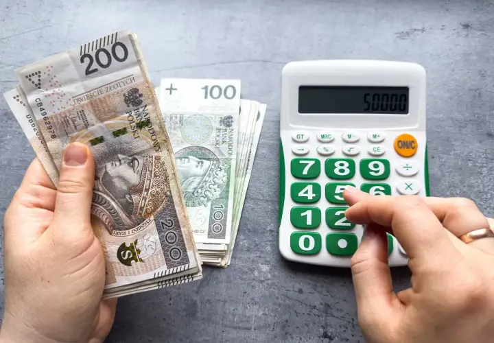 Ręka trzyma polskie banknoty 200 zł i 100 zł, obok kalkulator z wyświetloną kwotą 50000. Obliczenia pokazują, ile pracodawca płaci za pracownika przy najniższej krajowej.