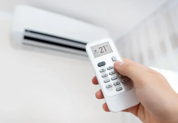 Mano ajustando el control remoto del aire acondicionado a 21°C en modo cooling. Perfecto para el heat cool en español.