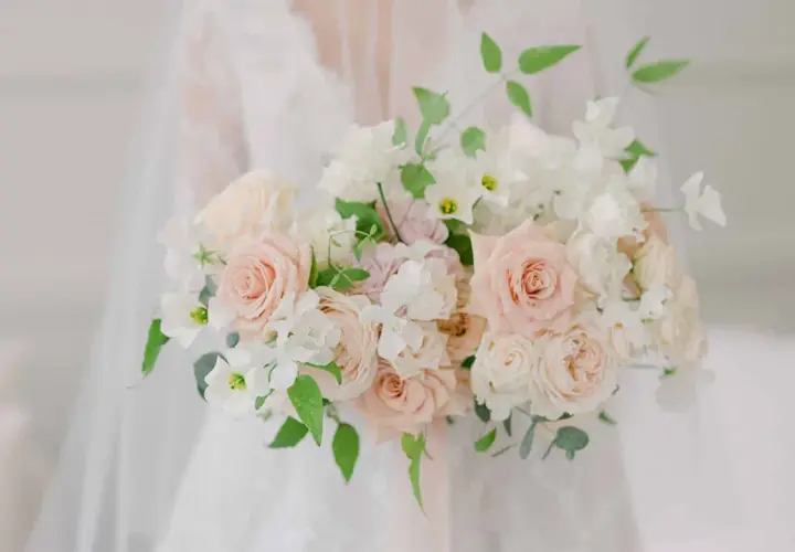Un bouquet de mariée tombant original, composé de roses douces et de fleurs blanches délicates, drapé sur une robe de mariée.