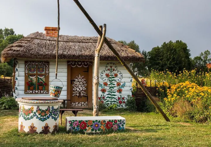 Kolorowy dom z malowanymi kwiatami, studnia i ławka. Zalipie atrakcje zachwycają ludowym pięknem.