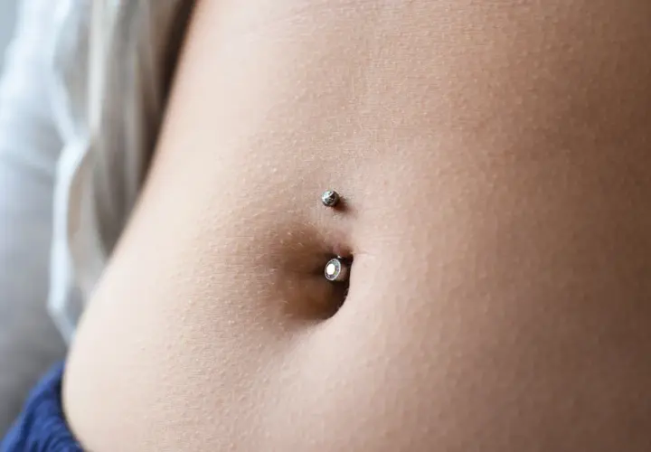 Zbliżenie na brzuch z kolczykiem w pępku. Delikatna skóra, subtelny blask biżuterii. To jest właśnie ten słynny **angie piercing**.