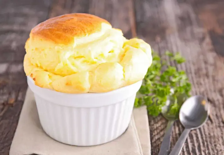 Un délicieux soufflé au fromage, doré et gonflé, servi dans un ramequin blanc sur une table en bois rustique.