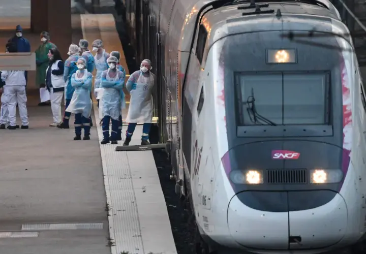 Grupa osób w kombinezonach ochronnych stoi na peronie obok pociągu SNCF.