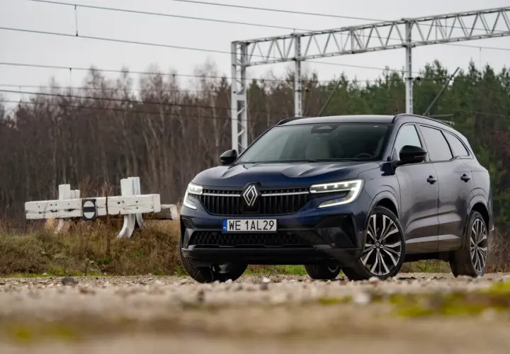Nowy Renault Espace 2024, ciemnoniebieski SUV, zaparkowany przy torach kolejowych, gotowy na przygodę.