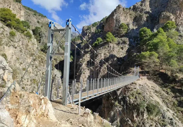 Puente colgante en la ruta del saltillo, con imponentes montañas rocosas y vegetación verde.