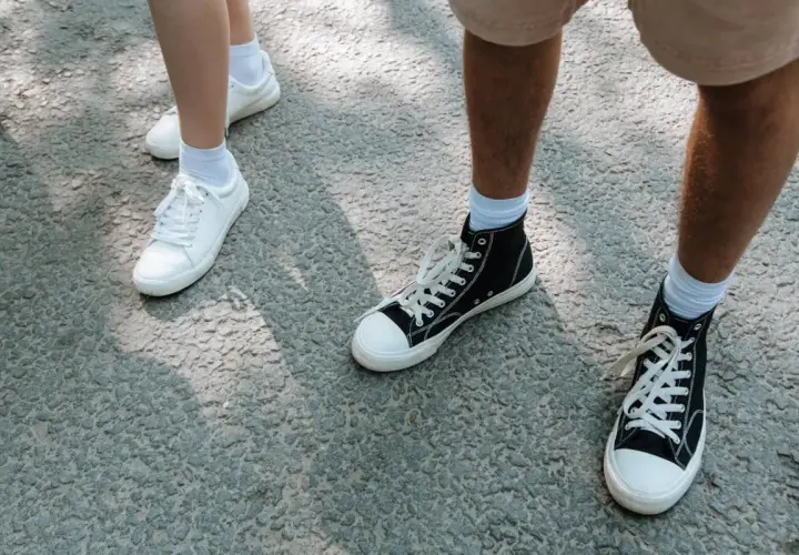 Białe i czarne trampki, idealne buty na długie marsze, stoją na szarej nawierzchni.