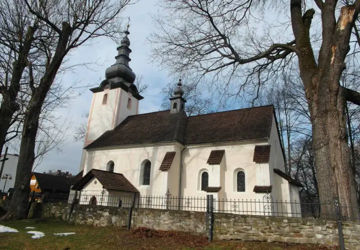 Kościół w Krościenku nad Dunajcem, z charakterystyczną wieżą i dachem, otoczony drzewami.