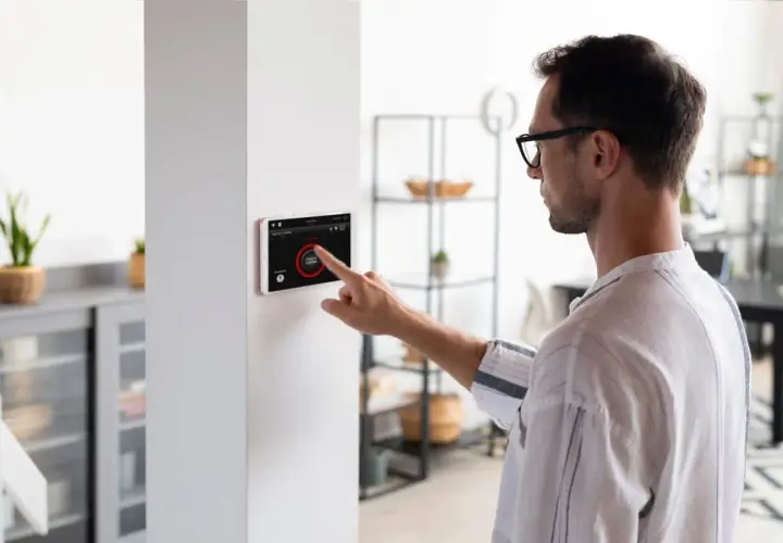 Hombre interactúa con pantalla táctil de domótica, controlando luces y seguridad. Los sensores domotica hacen el hogar inteligente.