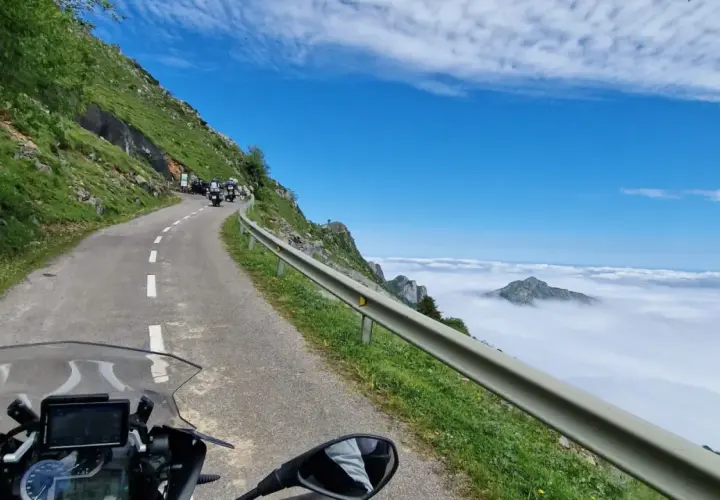 Motociclistas en un viaje por carretera, con un paisaje montañoso y nubes. El significado de este trip km es la aventura.