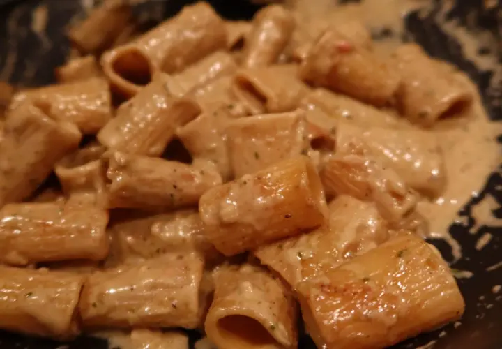 En närbild på rigatoni pasta i en krämig ost och skinksås. Pastan är täckt av såsen som ser smakrik ut.