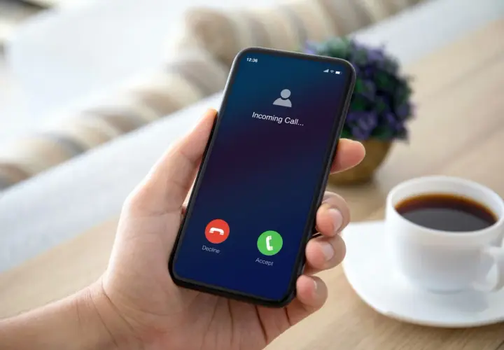 Dłoń trzyma smartfon z ekranem połączenia przychodzącego.