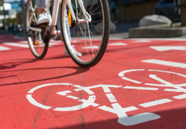 Rowerzysta nabiera prędkości na czerwonej ścieżce rowerowej, gdzie białe symbole rowerów wyznaczają trasę.